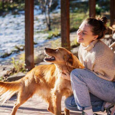 A happy young woman petting her golden retriever on a sunny porch, symbolizing the joy of a healthy diet with CHARM® Pet Food’s beef-flavored dry food.