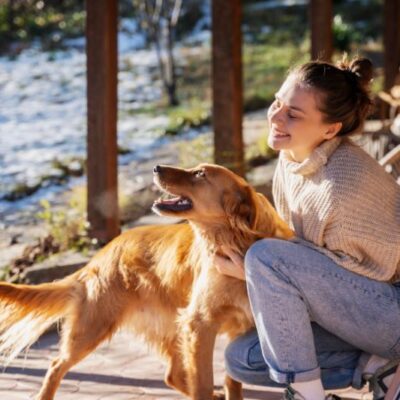 A happy young woman petting her golden retriever on a sunny porch, symbolizing the joy of a healthy diet with CHARM® Pet Food’s beef-flavored dry food.